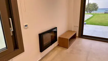 Wohnbereich mit modernem Wandkamin und großem Fenster mit Blick ins Grüne und zum Meer.