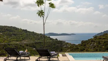 Entspannender Poolbereich mit Liegestühlen und weitem Blick auf das Meer und die umliegende grüne Landschaft.