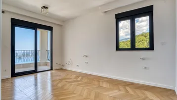 Geräumiges Zimmer mit Fischgrätparkett, Balkonzugang und einem Fenster mit Blick ins Grüne.
