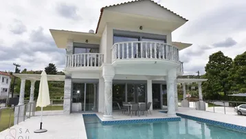 Moderne Villa mit großem Poolbereich und Balkonen, umgeben von gepflegten Grünflächen.