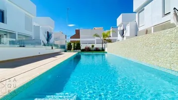 Großer Gemeinschaftspool mit Holzdeck und modernen weißen Gebäuden unter blauem Himmel.