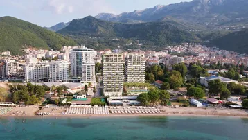 Luftaufnahme eines modernen Wohnkomplexes am Meer mit Strand und Bergen im Hintergrund.