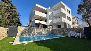 Modernes Apartmentgebäude mit Außenpool und gepflegtem Rasen unter blauem Himmel.