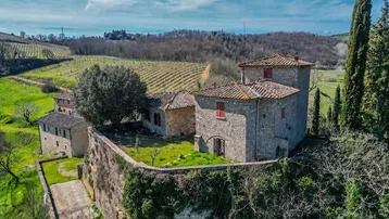 Historisches Steingebäude mit Terrakottadach inmitten einer malerischen Landschaft mit Weinbergen und Zypressen.