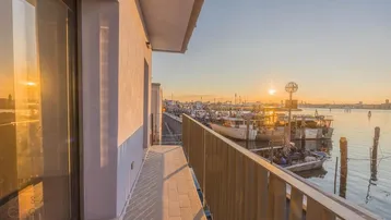 Geräumiger Balkon mit Fliesenboden und atemberaubendem Blick auf den Hafen bei Sonnenuntergang.