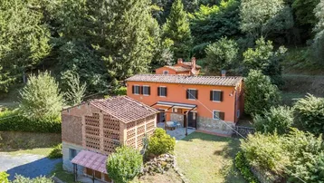 Traditionelles Landhaus mit Terrakottadachziegeln, umgeben von üppiger grüner Vegetation und Bäumen.