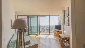 Helles Wohnzimmer mit Holzboden, großen Fenstern und weitem Blick über die Stadt bis zum Meer.