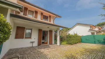 Vorderansicht des Hauses mit gepflasterter Auffahrt und grüner Hecke unter blauem Himmel.