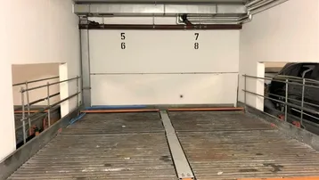 Tiefgaragenstellplatz mit Doppelparker-System für zwei Fahrzeuge und sichtbaren Installationen.
