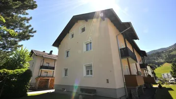 Sonnenbeschienene Fassade eines Mehrfamilienhauses mit Balkonen und gepflegtem Rasen.