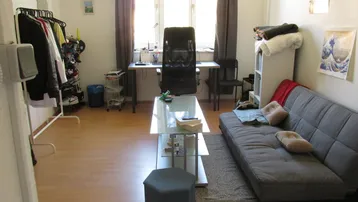 Helles Zimmer mit Schlafsofa, Schreibtisch und Kleiderstange, ideal für Studenten oder Singles.