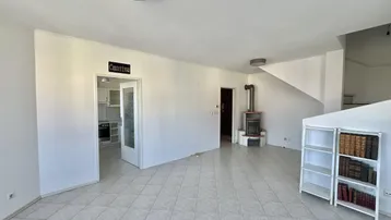 Geräumiges leeres Wohnzimmer mit Kaminofen, Fliesenboden und Zugang zur Küche.