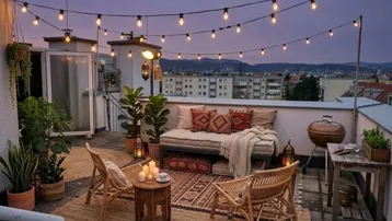 Gemütliche Dachterrasse am Abend mit Lichterketten, bequemen Sitzgelegenheiten und Grillbereich.