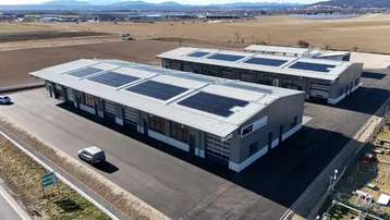 Luftaufnahme von zwei modernen Industriegebäuden mit Solarmodulen auf den Dächern, umgeben von Feldern.