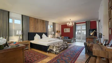 Geräumiges Schlafzimmer mit Holzwand, rotem Akzent und gemütlichem Sitzbereich sowie Schreibtisch.