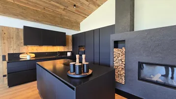 Exklusive schwarze Küche mit Kochinsel, integriertem Kamin und Holzregal für Brennholz.