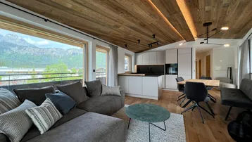 Modernes offenes Wohnzimmer mit Holzbalkendecke, integrierter Küche und beeindruckendem Bergblick.