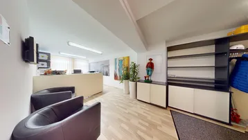 Empfangsbereich eines Büros mit beigen Theken, dunklen Ledersesseln und hellem Holzboden.