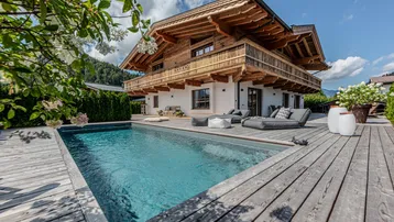 Luxuriöses Chalet mit privatem Pool, Holzterrasse und atemberaubendem Bergblick unter blauem Himmel.