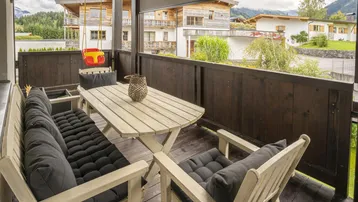 Gemütlicher Balkon mit Holztisch, Sitzgelegenheiten und Blick auf die umliegenden Häuser.