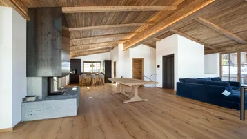 Geräumiger offener Wohnbereich mit Kamin, Holzbalkendecke und Essbereich, ideal für geselliges Beisammensein.