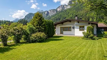 Gepflegter Garten mit Rasenfläche und Sträuchern vor einem Haus mit Bergblick.