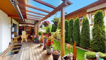 Überdachte Holzterrasse mit Pflanzen und Zugang zum gepflegten Gartenbereich.