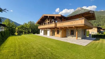Großzügiger Gartenbereich mit gepflegtem Rasen und moderner Chalet-Architektur im Hintergrund.