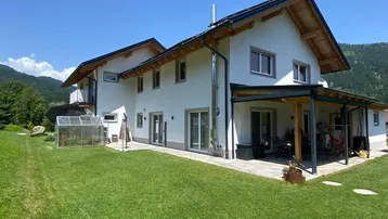 Modernes Einfamilienhaus mit großem Garten, überdachter Terrasse und Bergblick.
