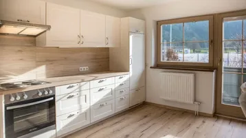 Helle Küche mit weißen Schränken, Holzoptik-Arbeitsplatte und Blick ins Grüne.
