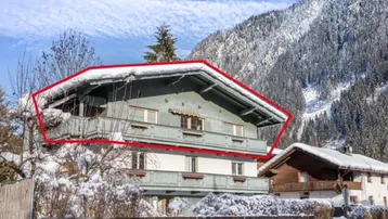 Traditionelles Gebäude in den Bergen mit Holzbalkonen und schneebedeckter Umgebung.