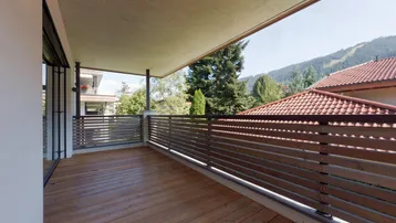 Geräumiger  überdachter Balkon mit Holzboden und Holzgeländer, bietet einen weiten Blick auf die Berge.
