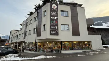 Modernes Geschäftsgebäude mit mehreren Etagen und großen Schaufenstern, umgeben von Schnee und Bergen.