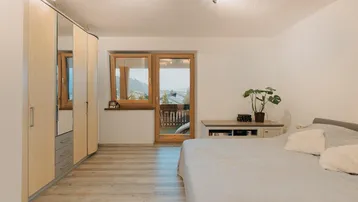 Schlafzimmer mit Doppelbett, Kleiderschrank und Zugang zum Balkon mit Bergblick.
