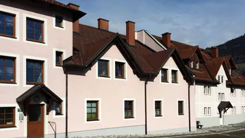 Reihenhäuser mit hellrosa Fassaden, braunen Ziegeldächern und Blick auf die umliegende Landschaft.
