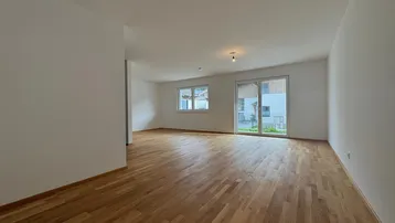 Helles, leeres Zimmer mit Holzboden und Zugang zu einem Außenbereich, ideal als Wohnzimmer.