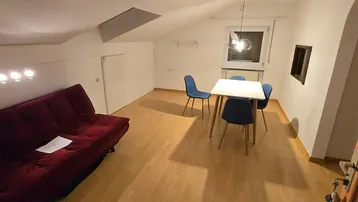 Gemütlicher Wohn-Essbereich im Dachgeschoss mit rotem Sofa und Esstisch für gesellige Stunden.