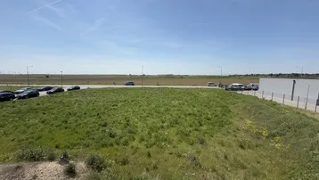 Weitläufiges, unbebautes Grundstück mit Grasfläche und Blick auf umliegende Gebäude und Parkplätze.