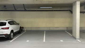 Helle Tiefgarage mit markierten Parkplätzen und Betonwänden, ein Fahrzeug ist bereits geparkt.