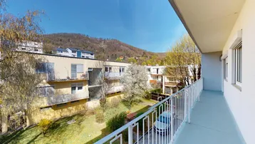 Langer Balkon mit Blick auf die umliegenden Gebäude und bewaldeten Hügel unter blauem Himmel.