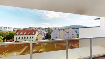 Balkon mit Glasgeländer und weitem Blick über die Dächer der Stadt und grüne Hügel.