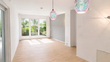 Helles Wohnzimmer mit großen Fenstern, Holzboden und modernen Hängelampen.