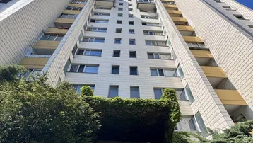 Hohes Wohngebäude mit weißer Fassade und begrüntem Eingangsbereich unter blauem Himmel.