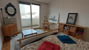 Helles Schlafzimmer mit Bett, Schreibtisch und Zugang zum Balkon, freundlich eingerichtet.