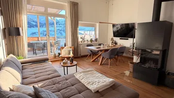 Helles Wohn- und Esszimmer mit Kamin, Holzboden und Zugang zum Balkon mit Bergblick.