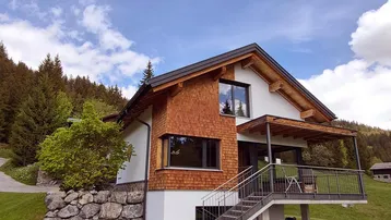 Modernes Haus mit Holzfassade und großzügiger Terrasse in alpiner Landschaft.