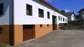 Vorderansicht eines ländlichen Gebäudes mit weißer Fassade, braunem Sockel und rotem Ziegeldach.