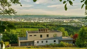 Modernes Gebäude mit Flachdach und weitem Blick über die Stadt und die umliegende Landschaft bis zu den Bergen.