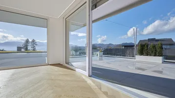 Helles Wohnzimmer mit Fischgrätparkett und großen Schiebetüren zur Terrasse mit Seeblick.