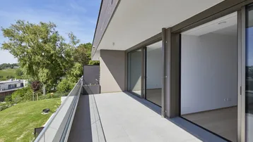 Geräumiger Balkon mit Fliesenboden, Glasgeländer und weitem Blick ins Grüne und auf die Umgebung.